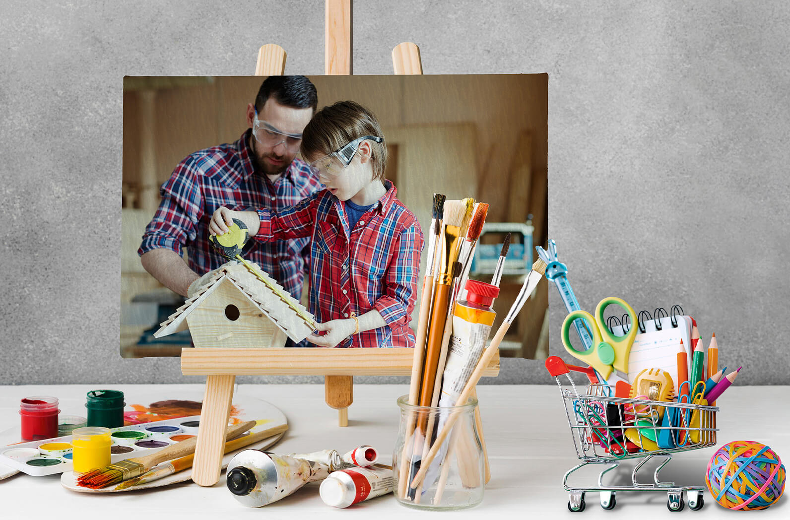  boyalar ve kalemlerin arkasında resim tuvalinin içinde Bir kuş evi yapmak için çalışan baba ve oğlunun resmi